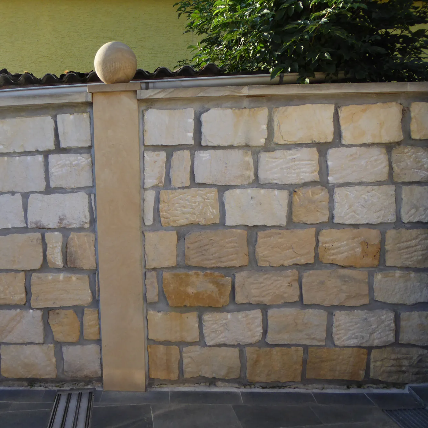 Gartenmauer aus gelben Sandstein-Mauersteinen im Bruchsteinverband mit Sandstein-Pfeiler, Abdeckplatte und Kugelaufsatz