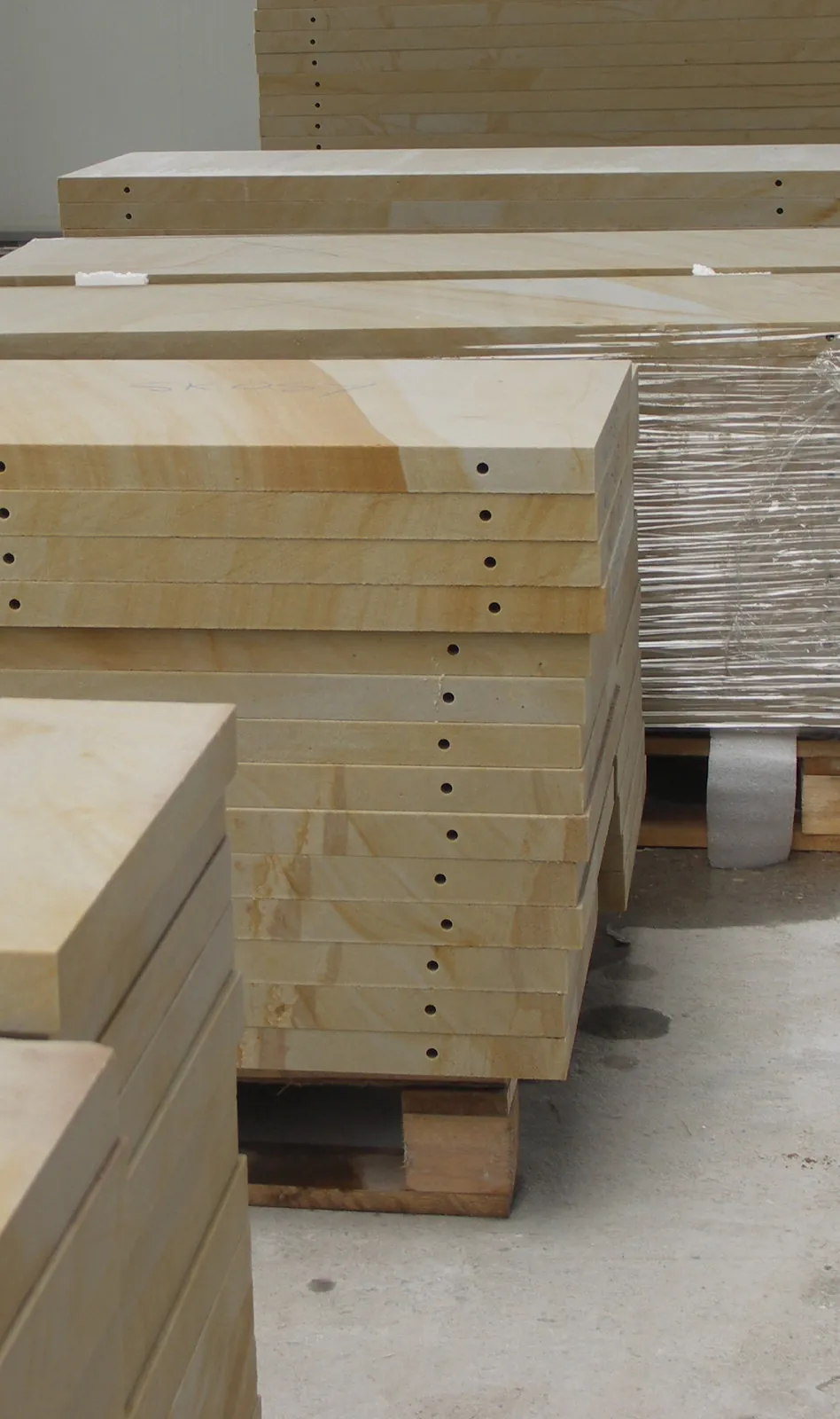 Gestapelte gelbe Sandstein-Fassadenplatten mit gebohrten Dübellöchern zur Hinterlüftung auf Lagerpaletten – Vorfertigung Werkstatt