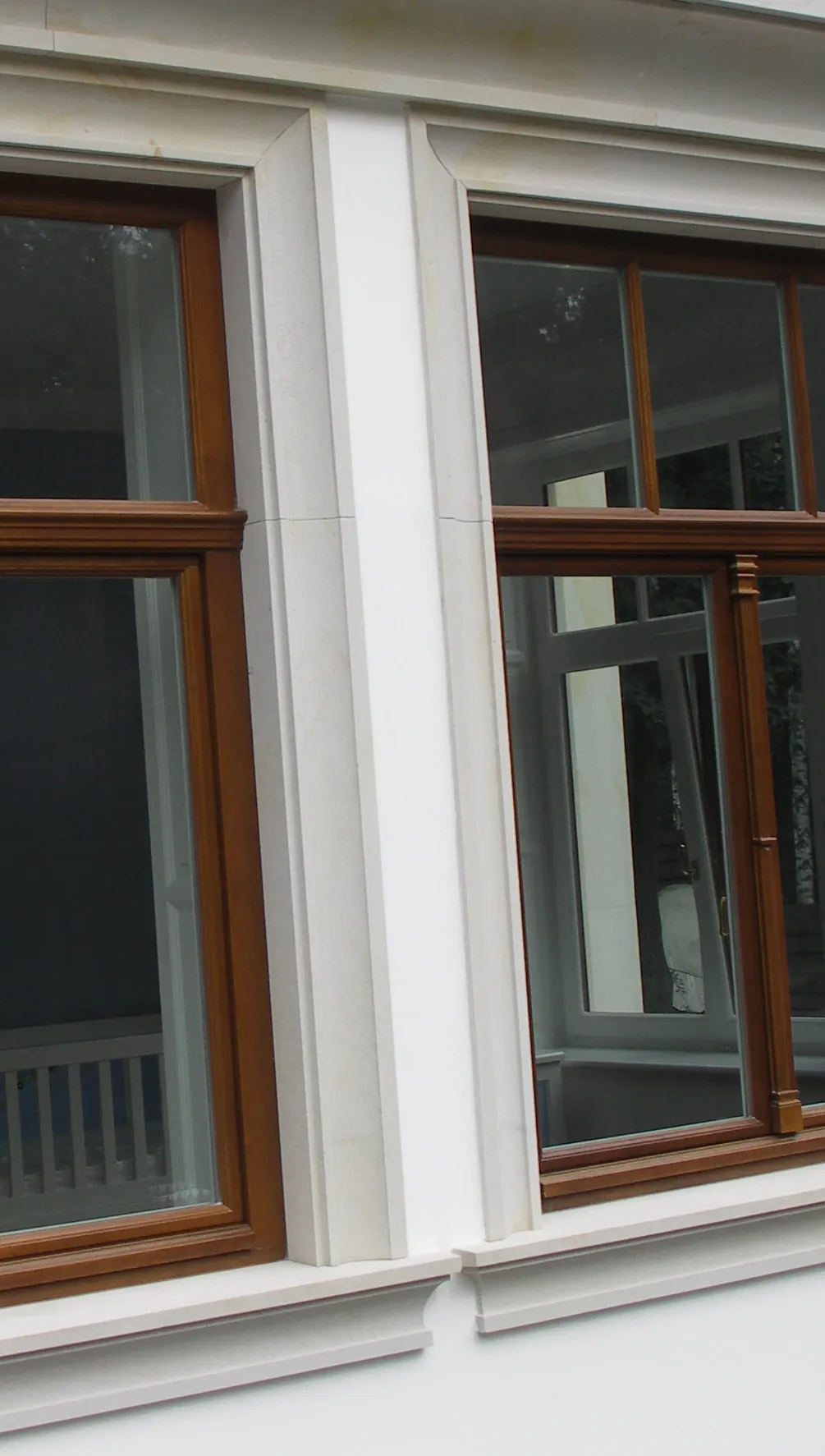 Heller Sandstein-Fensterpilaster mit abgeschrägter Deckplatte zwischen zwei Holzfenstern an verputzter Fassade, oben Sandstein-Gesims