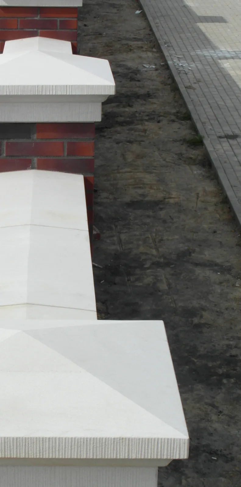 Helle Sandstein-Mauerabdeckungen mit pyramidaler Zeltdachform und gestock­ter Randkante auf gemauerten Backsteinpfeilern – Draufsicht Reihenanordnung