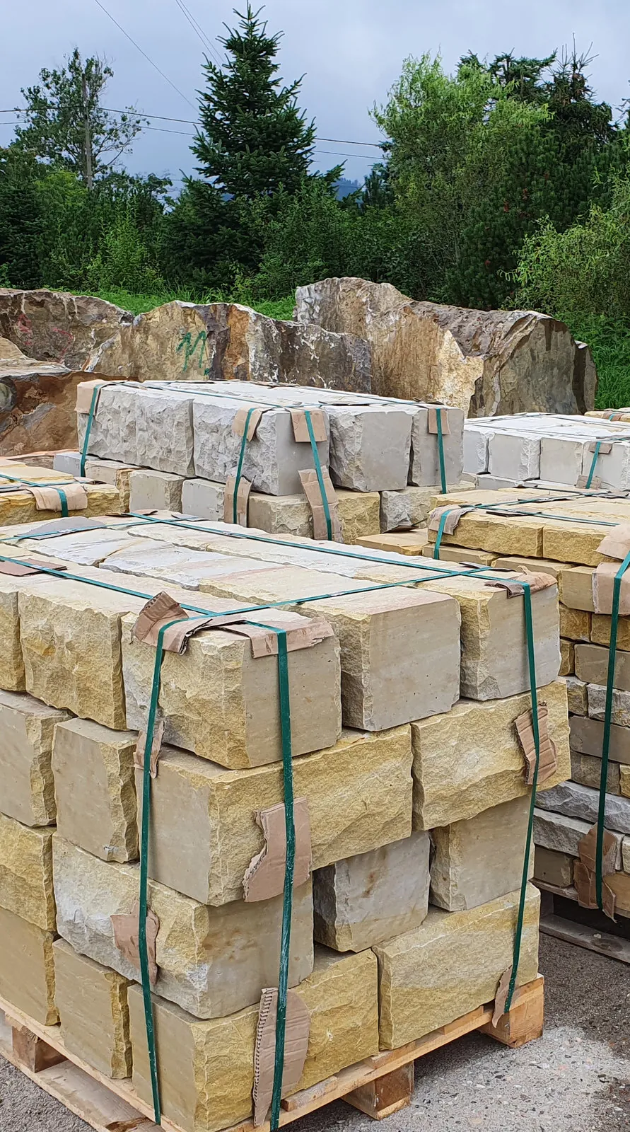 Gelbe Sandstein-Mauersteine mit Bruchsteinoberfläche auf Lieferpaletten mit Spanngurten gesichert – Werkslager Versandbereit