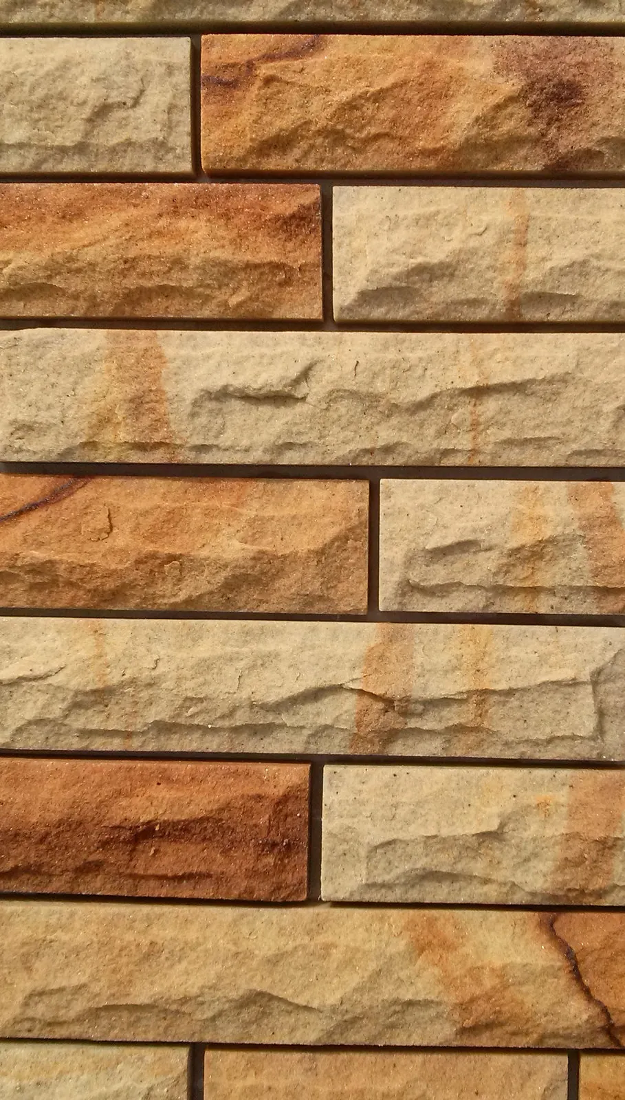 Gelbe Sandstein-Riemchen mit gespaltener Steinoberfläche im Läuferverband – Nahaufnahme Farbspektrum Beige bis Rostbraun