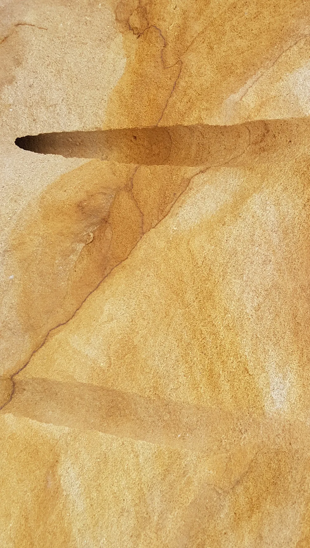 Gelber Sandstein-Rohblock mit Bohrloch und fließender Naturmaserung in Ockergelb und Beige – Nahaufnahme Steinoberfläche