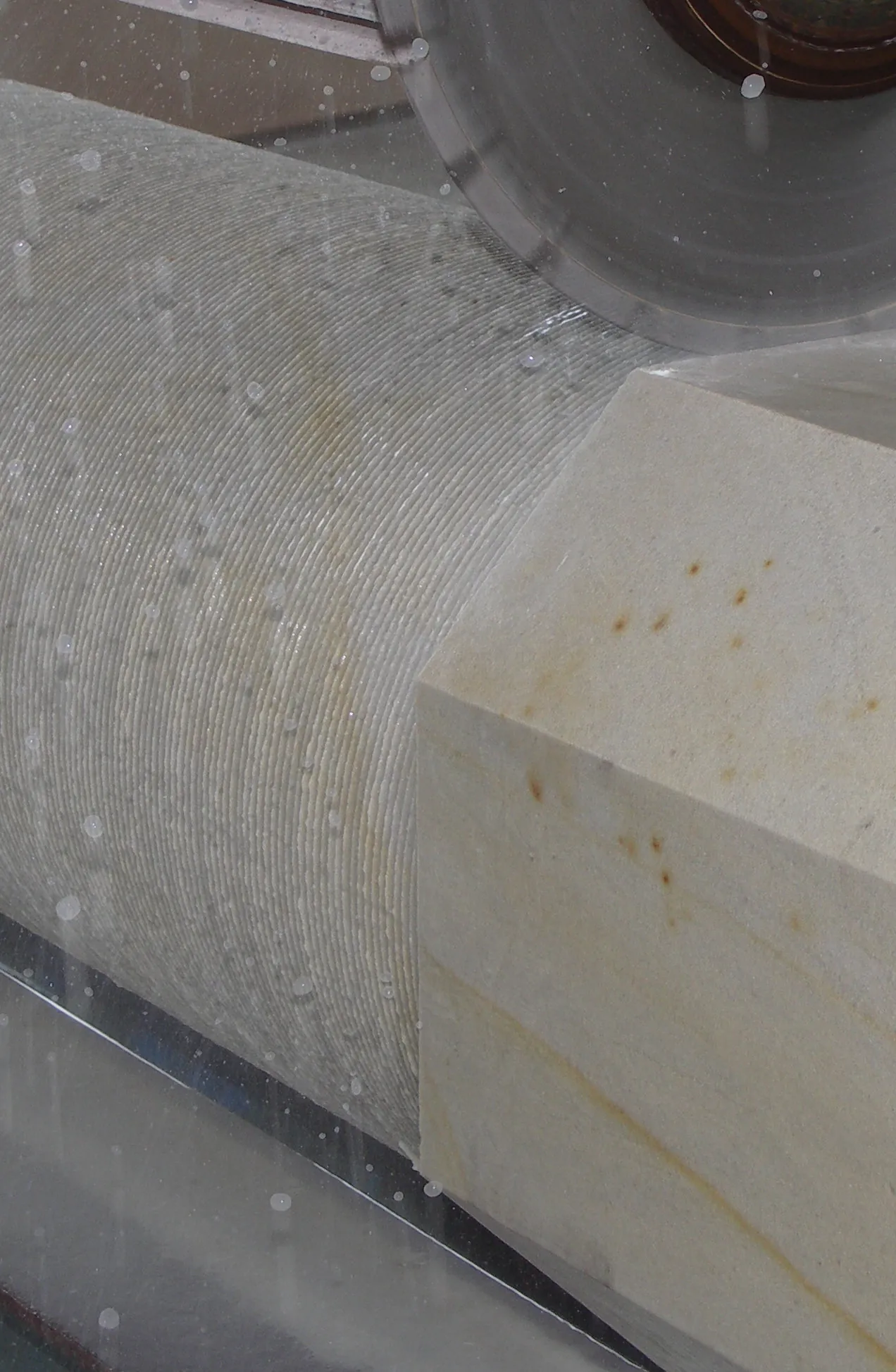 Heller Sandstein-Säulenschaft auf Steindrehbank in Bearbeitung – Nahaufnahme CNC-Rundprofilierung mit Kühlwasser im Werkstattbetrieb