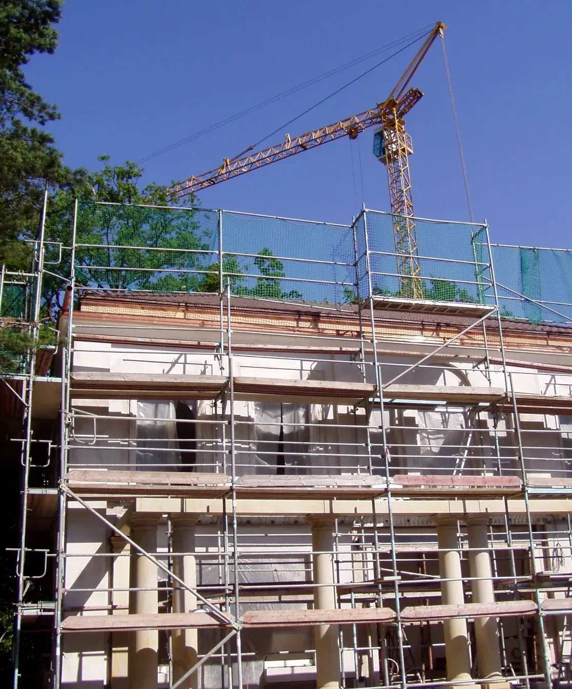Sandstein-Villenfassade im Bau mit Gerüst, sichtbaren Sandstein-Säulen und Gesimsen im Rohbauzustand, Baukran im Hintergrund