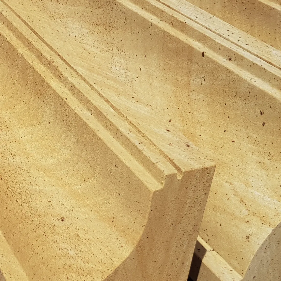 Warthauer Sandstein Gesimsprofil gestapelt – warmgelbe Steinoberfläche mit charakteristischer Eisenoxidpunktierung und präzisem Doppelnutprofil – Nahaufnahme Werkstattlager